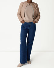 Modelo usando jaqueta de couro pelica rosa claro com suéter creme e calça jeans azul, visual casual elegante.