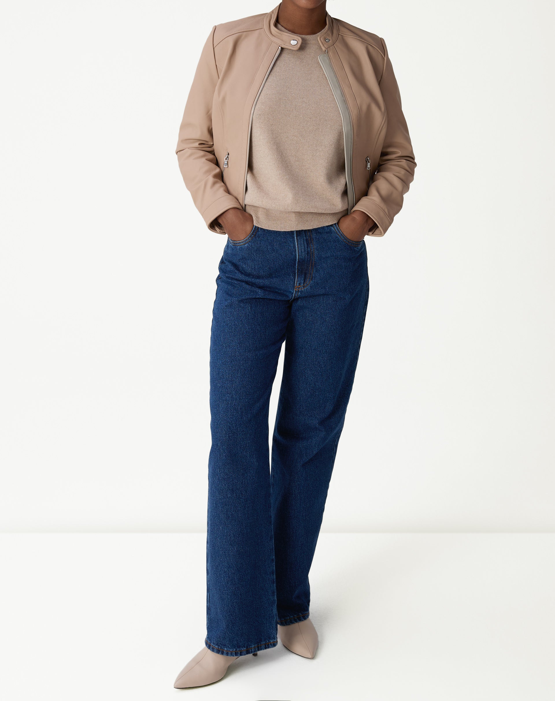 Modelo usando jaqueta de couro pelica rosa claro com suéter creme e calça jeans azul, visual casual elegante.