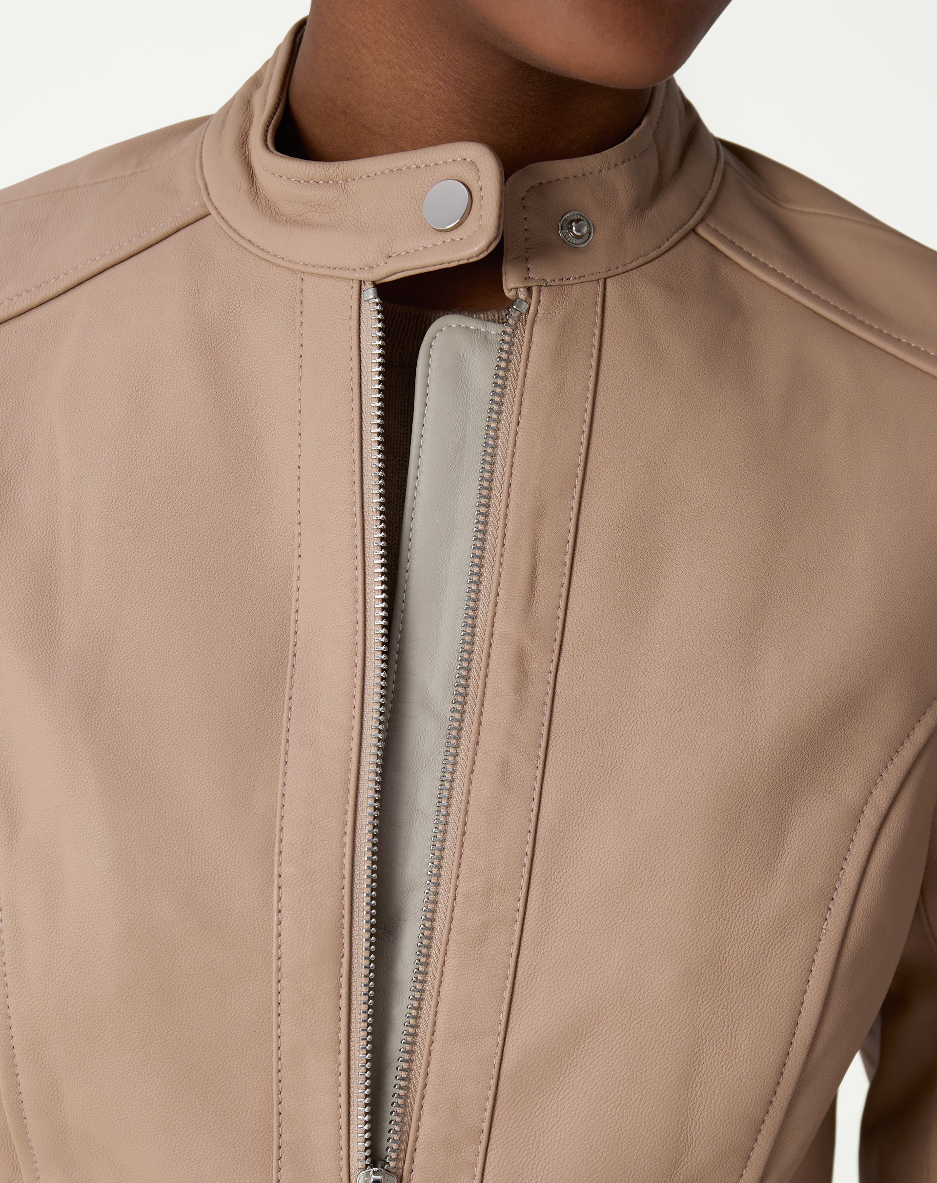 Fechamento do colarinho mandarim com botão de pressão e zíper central da jaqueta de couro pelica rosa claro.