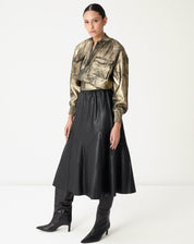 Saia midi preta em poliuretano vista frontal com recortes assimétricos e cós alto elástico, combinada com jaqueta metálica e bota de cano alto