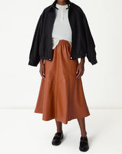 Modelo vestindo saia midi Statement em caramelo com recortes assimétricos, combinada com blusa branca e jaqueta preta.