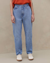 Modelo vestindo calça mom jeans azul clara com blusa laranja, vista lateral.