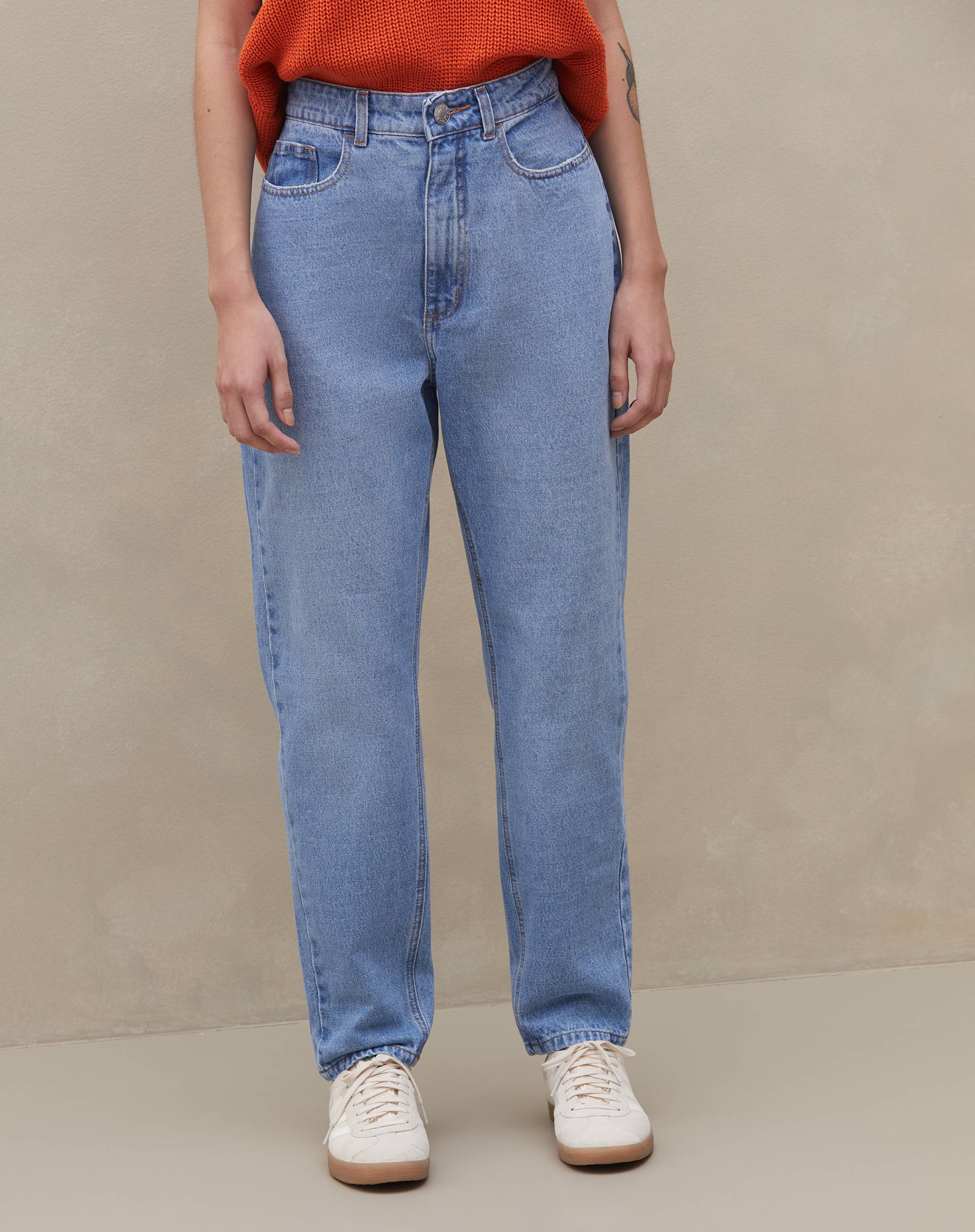 Modelo vestindo calça mom jeans azul clara com blusa laranja, vista lateral.