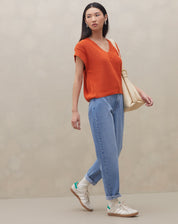 Modelo vestindo calça mom jeans azul clara com blusa laranja, vista traseira.