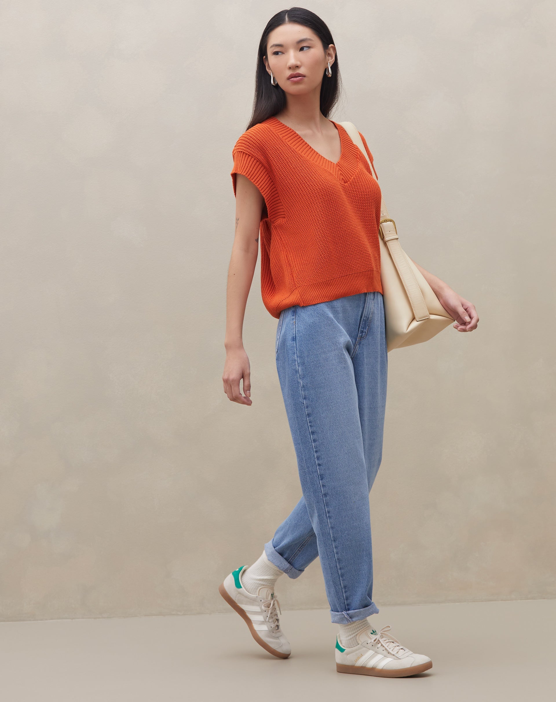 Modelo vestindo calça mom jeans azul clara com blusa laranja, vista traseira.