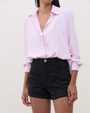 Modelo vestindo shorts de sarja preto com camisa rosa, mostrando o look completo.