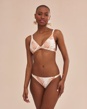 Modelo vestindo bottom de biquíni com estampa botânica em fundo bege, vista lateral.