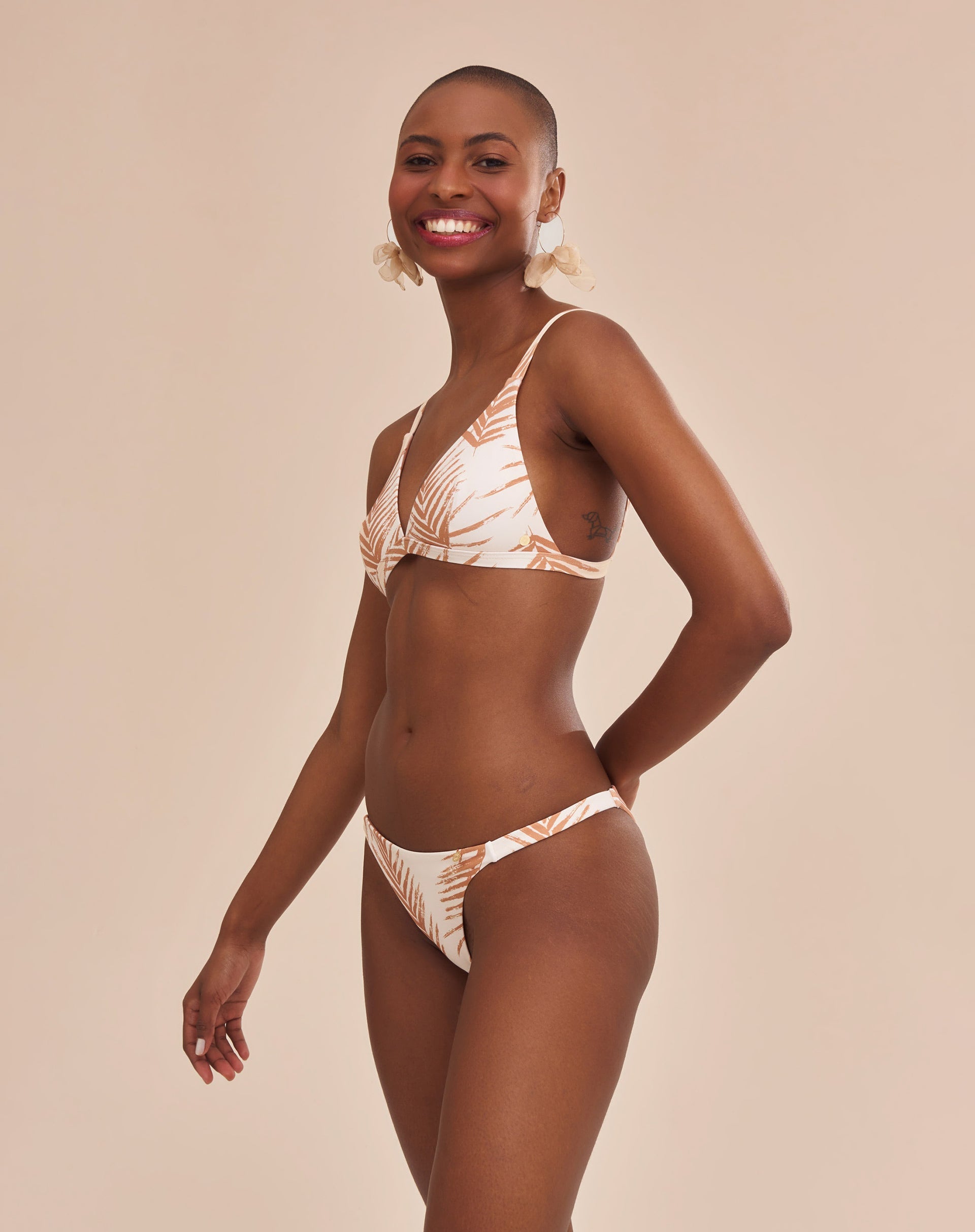 Modelo vestindo bottom de biquíni com estampa botânica em fundo bege, vista diagonal.