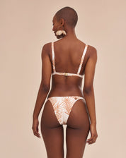 Modelo vestindo bottom de biquíni com estampa botânica em fundo bege, vista traseira.