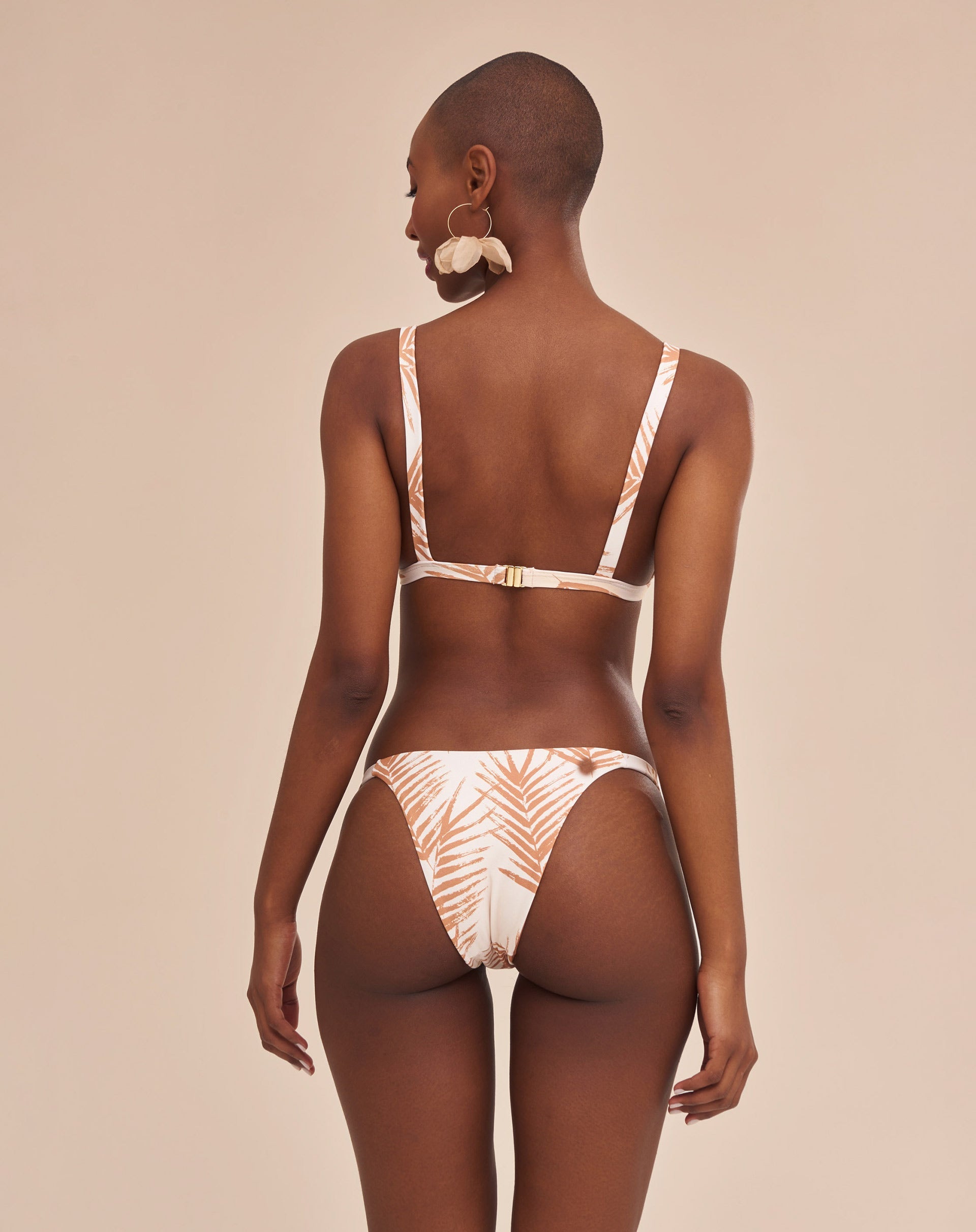 Modelo vestindo bottom de biquíni com estampa botânica em fundo bege, vista traseira.