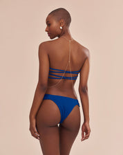 Top bandeau azul vibrante com franzido frontal e tiras entrelaçadas nas costas, visto de trás.
