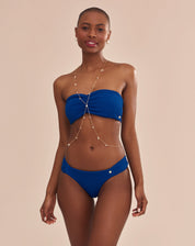 Calcinha de biquíni azul com laterais franzidas em modelo com pele escura vista lateral.