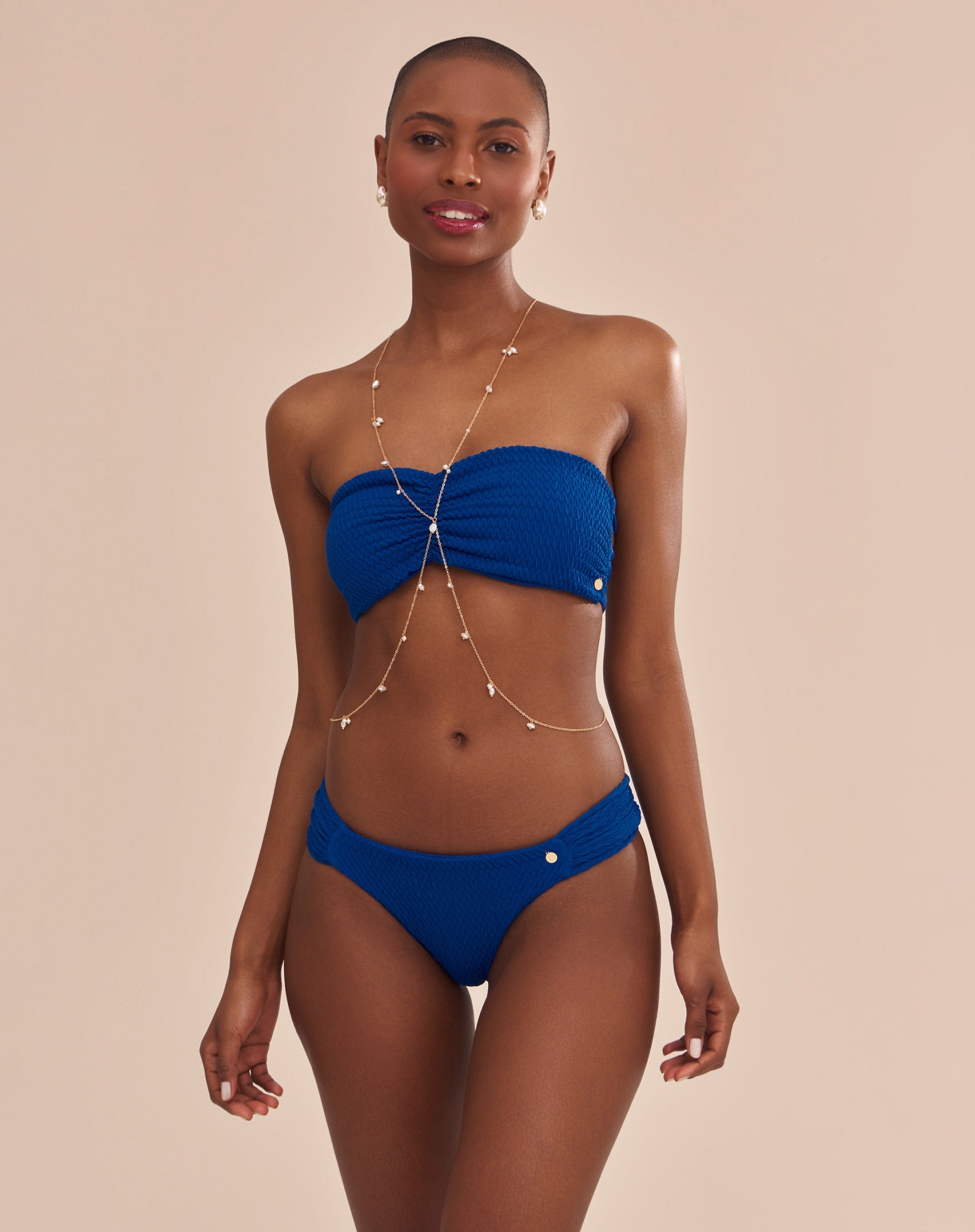 Calcinha de biquíni azul com laterais franzidas em modelo com pele escura vista lateral.