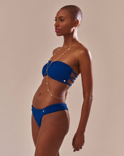 Calcinha de biquíni azul com laterais franzidas em modelo com pele escura vista traseira.