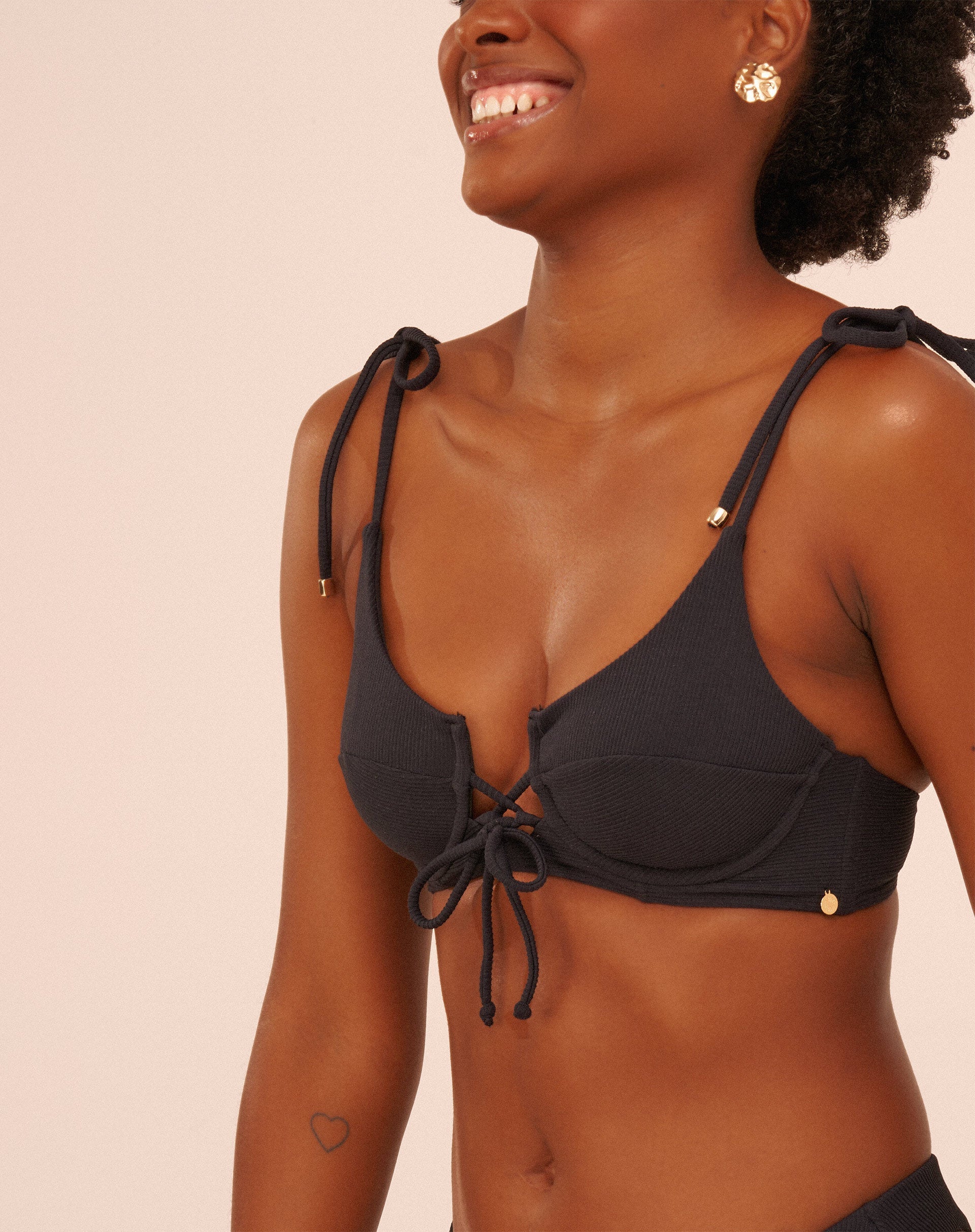 Detalhe do top de biquíni preto com aro e alças ajustáveis em forma de laço, close-up.