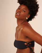 Vista lateral de um top de biquíni preto com entrelaçados laterais, mostrando detalhes do design.