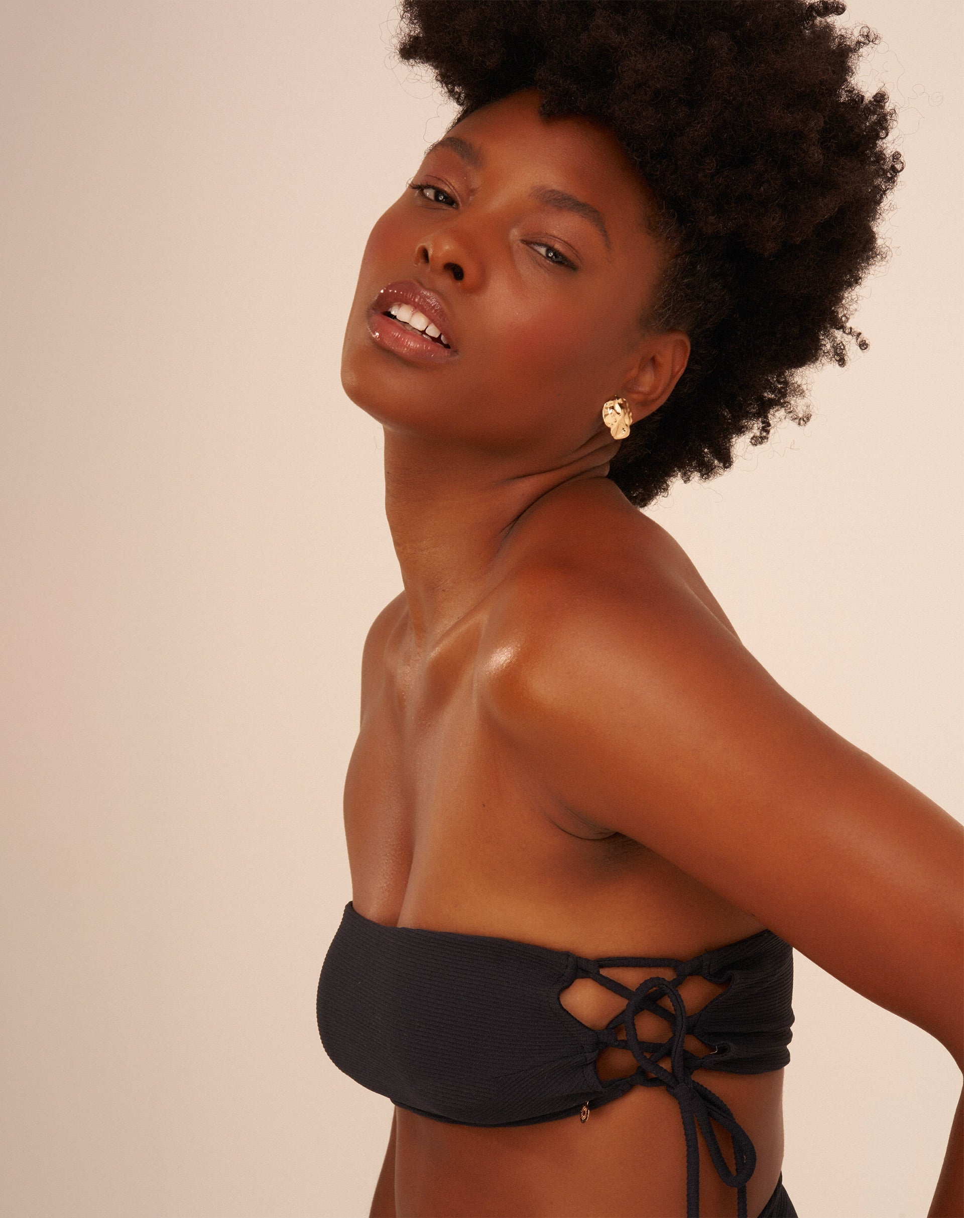 Vista lateral de um top de biquíni preto com entrelaçados laterais, mostrando detalhes do design.