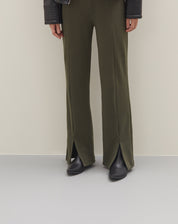 Imagem de uma pessoa vestindo calça verde com abertura frontal na barra, combinada com botas pretas.