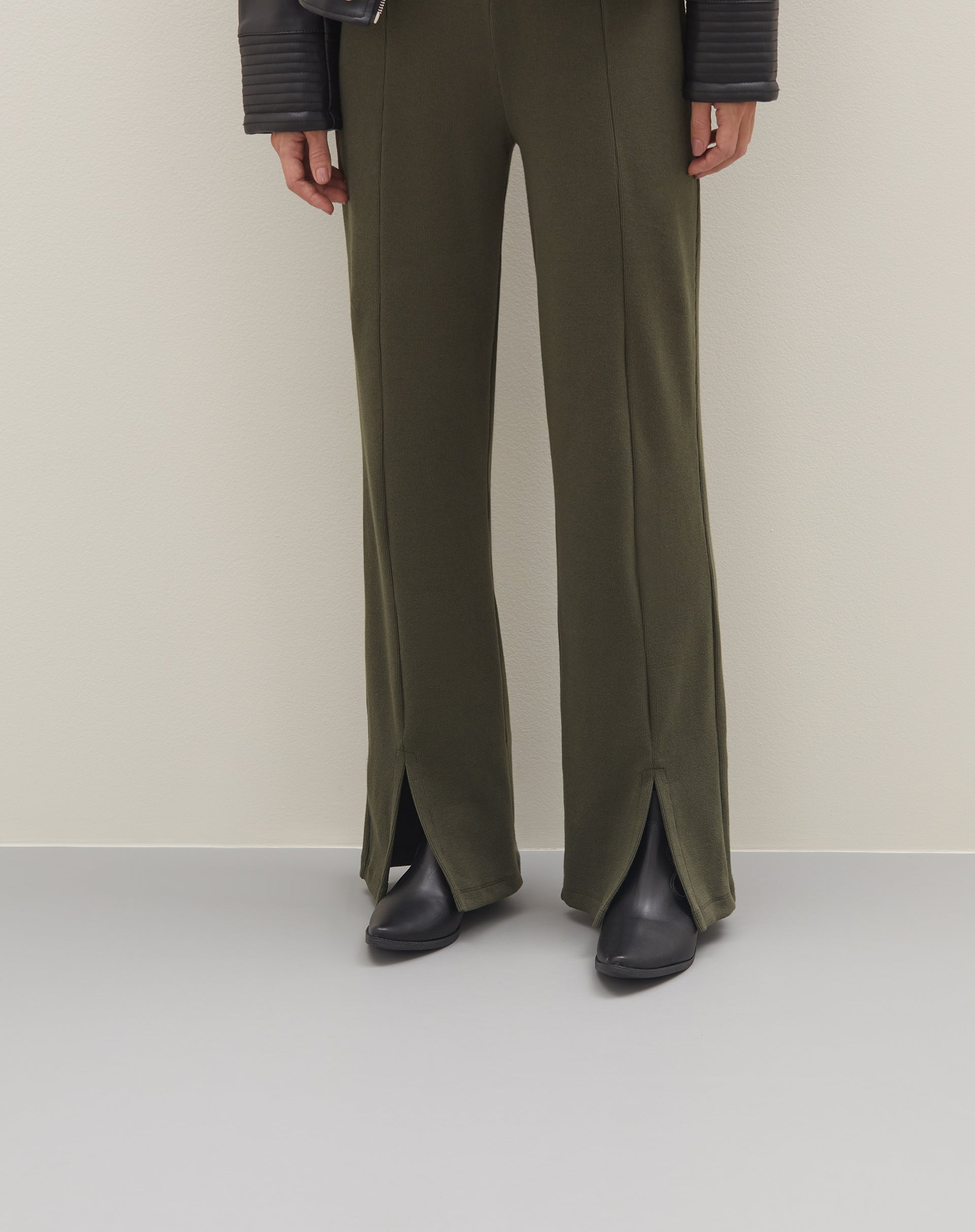 Imagem de uma pessoa vestindo calça verde com abertura frontal na barra, combinada com botas pretas.