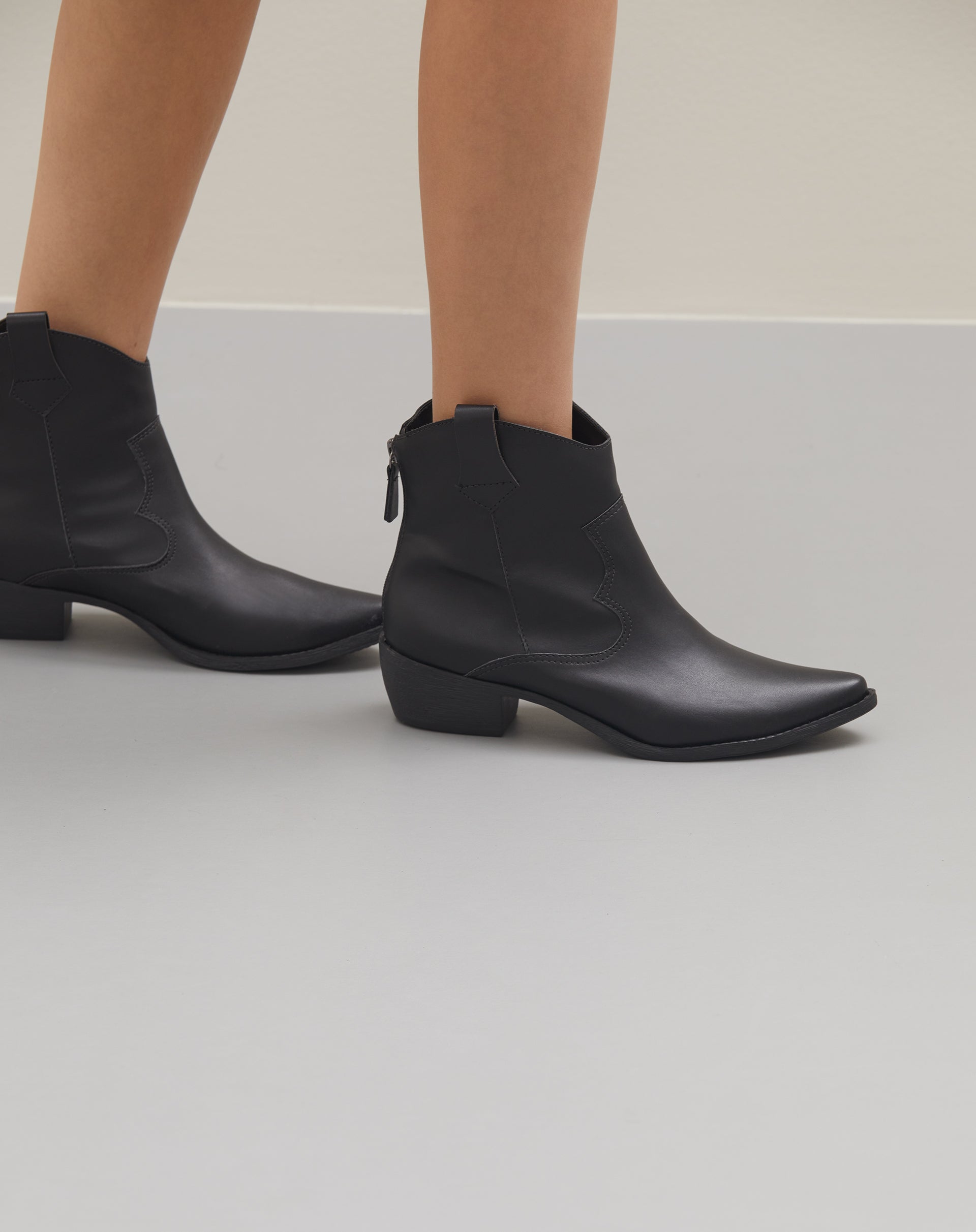 Imagem de uma bota preta estilo western com cano curto e salto bloco baixo.