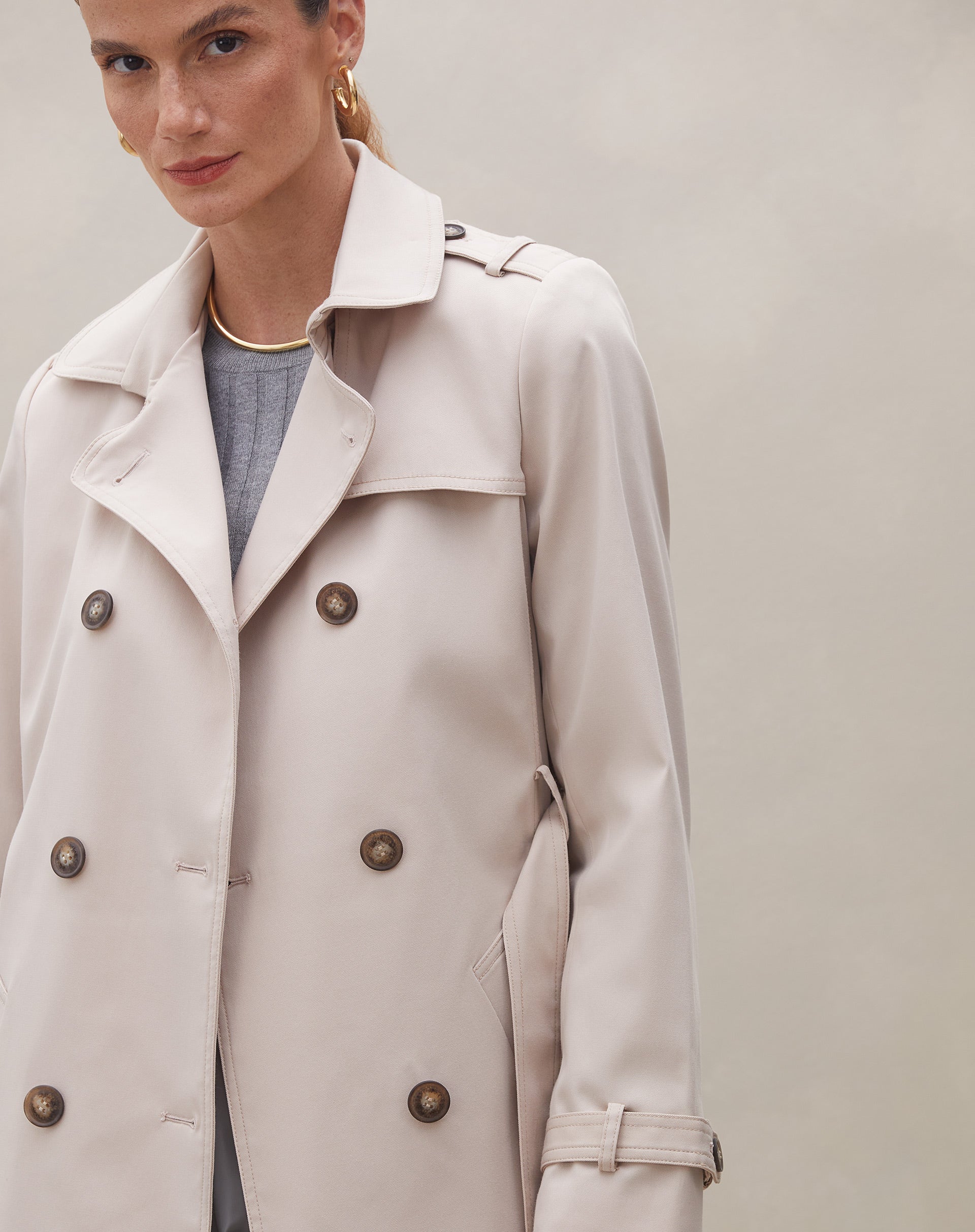 Modelo mostrando a parte traseira do trench coat bege com detalhes do cinto.