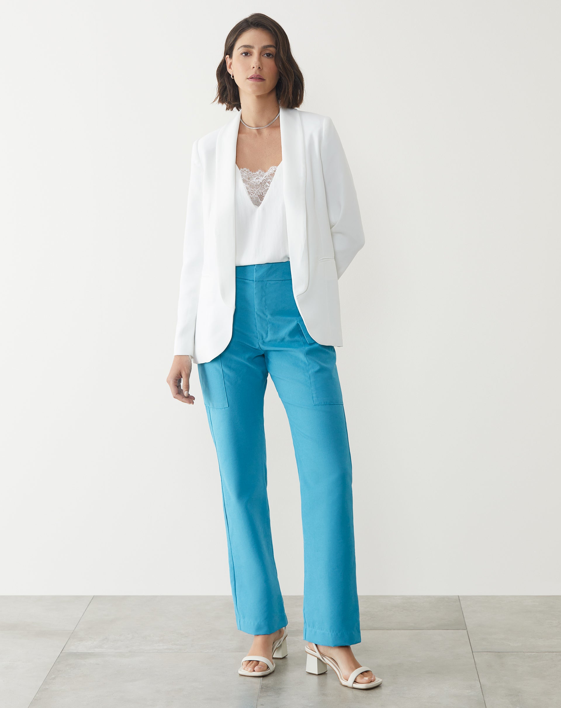 Modelo vestindo calça reta azul claro com blazer branco e sandálias.