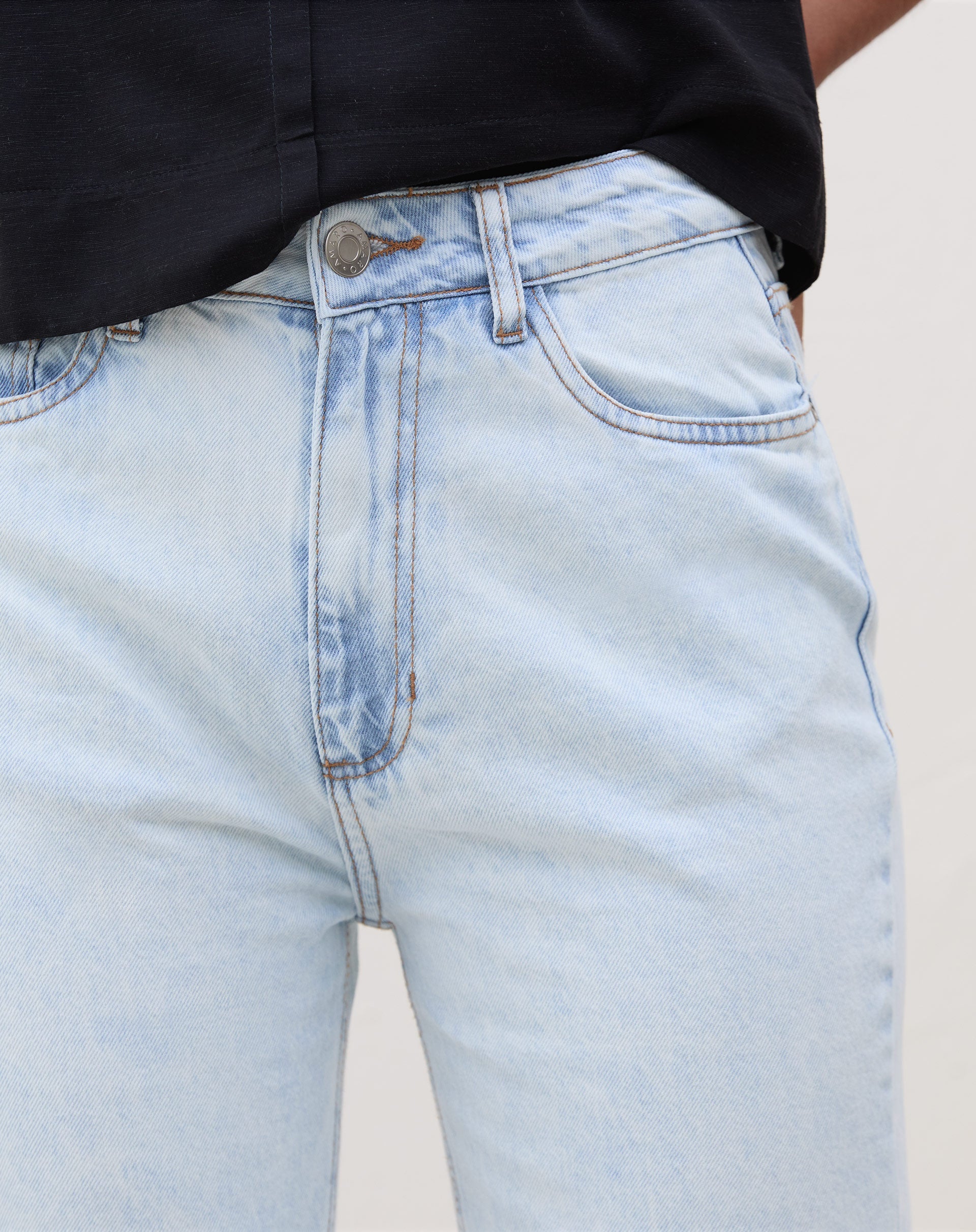 Detalhe do cós alto e fechamento com botão da calça slim jeans azul claro.