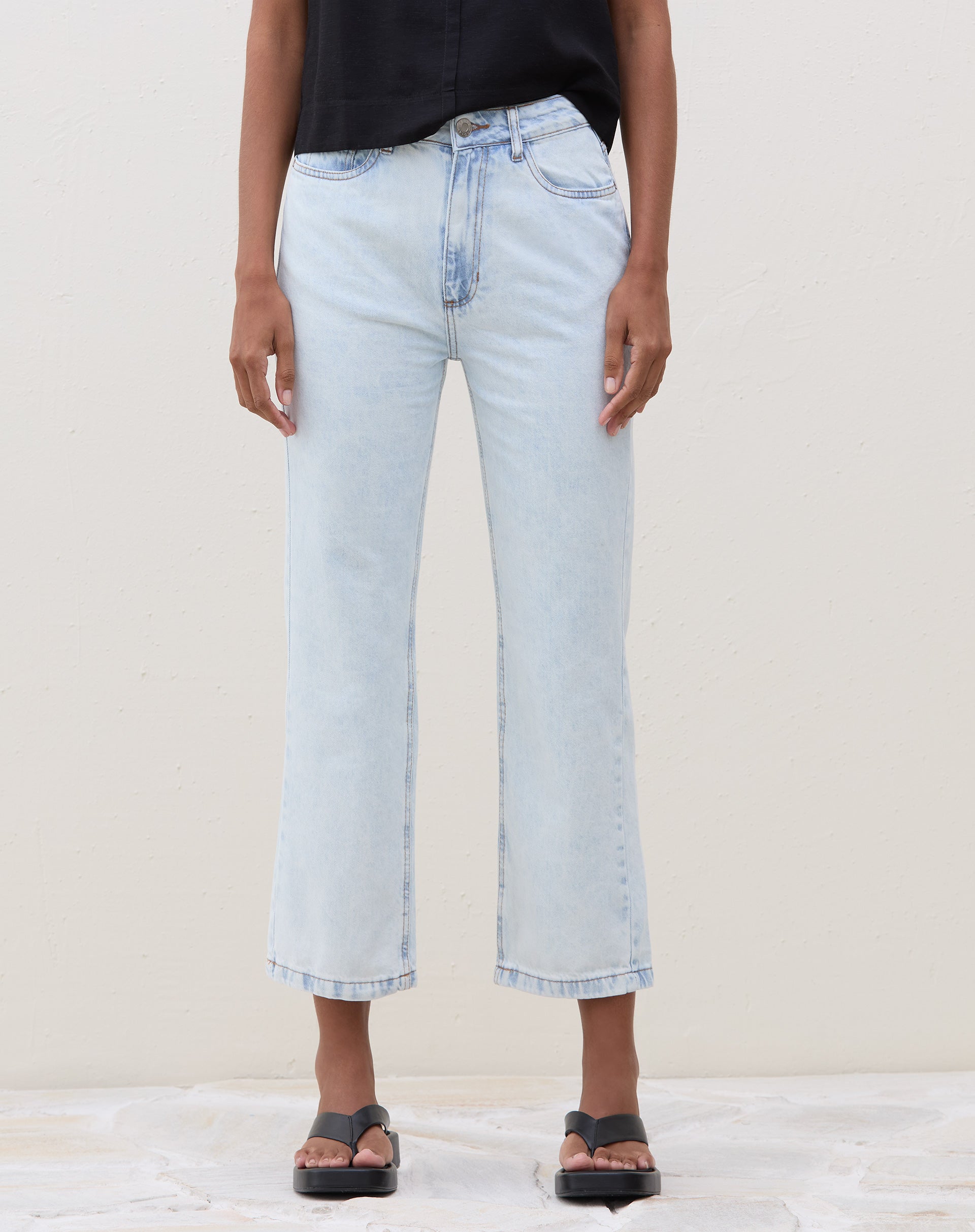 Modelo vestindo calça slim jeans azul claro com blusa preta, vista lateral.