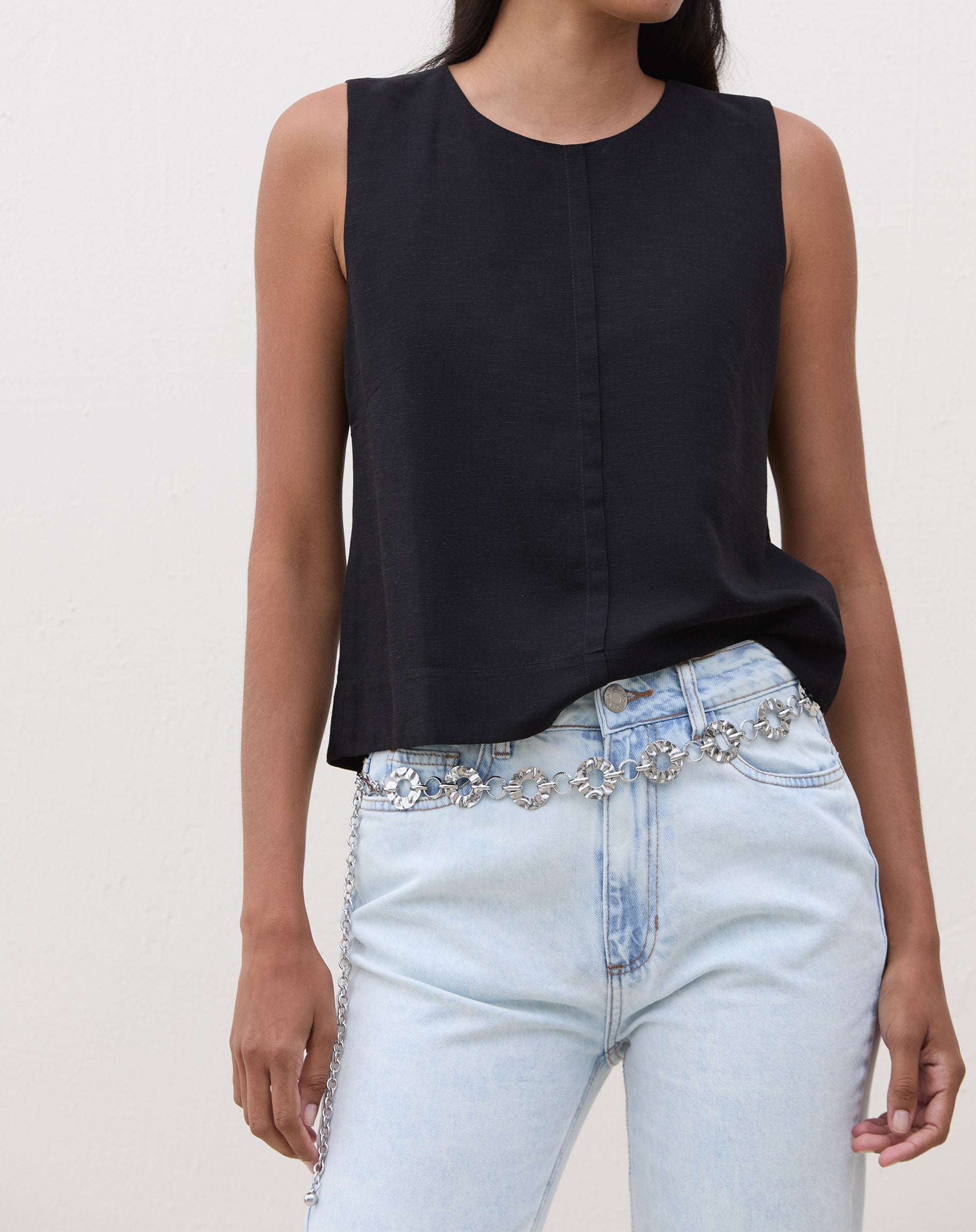 Modelo vestindo calça slim jeans azul claro com blusa preta e cinto decorativo.