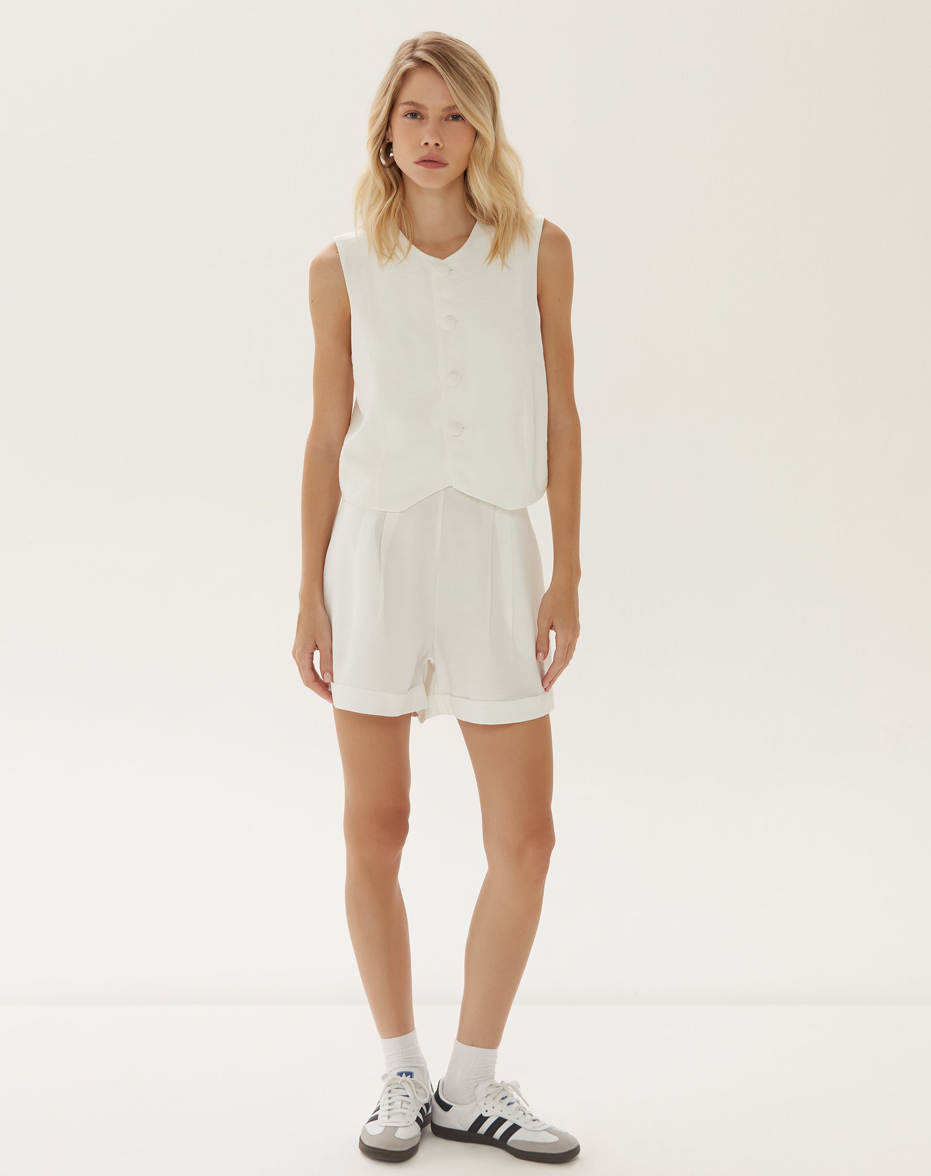 Modelo vestindo shorts de alfaiataria off-white com barra dobrada, vista frontal.