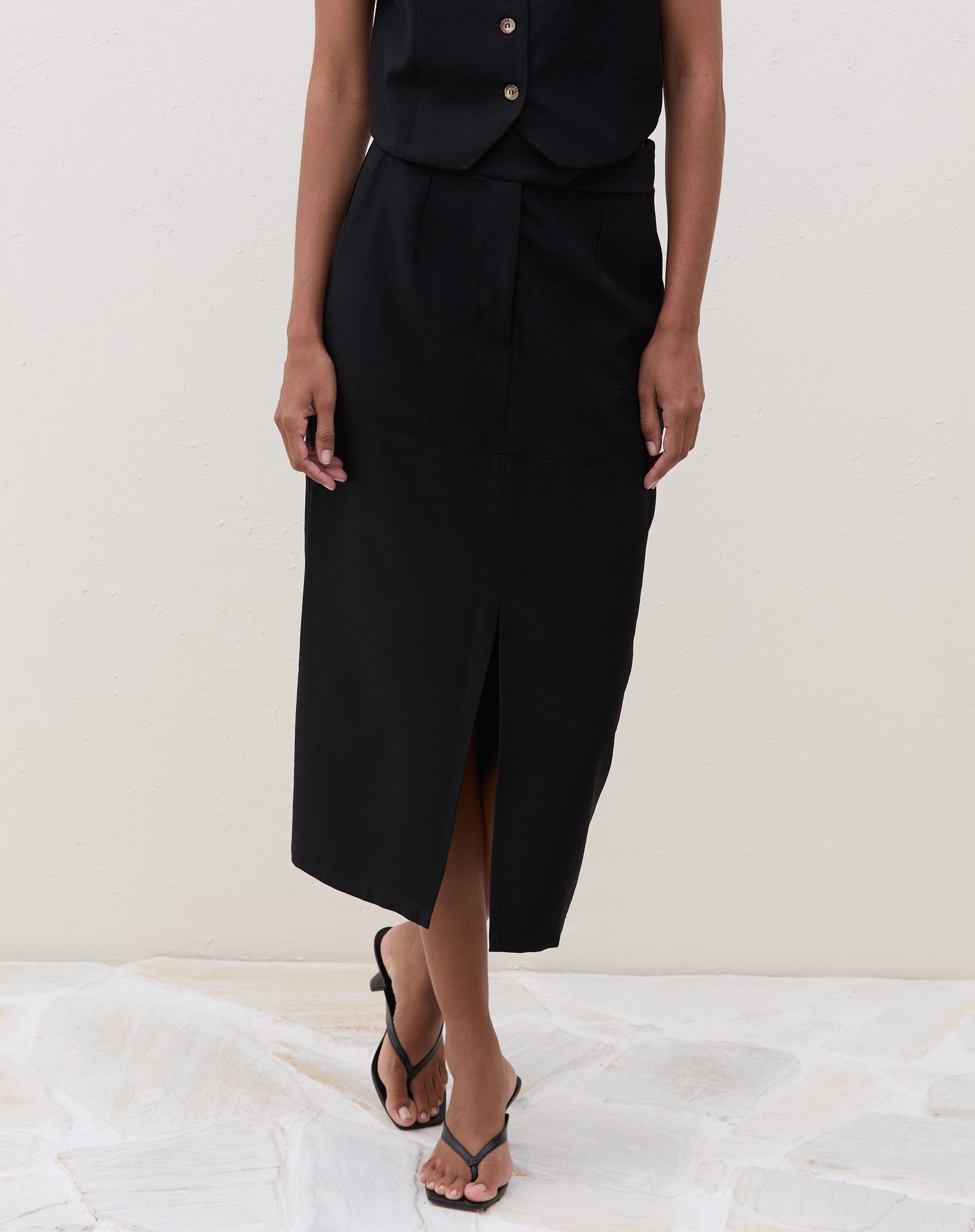 Detalhe da saia midi preta com fenda frontal, mostrando o ajuste na cintura.