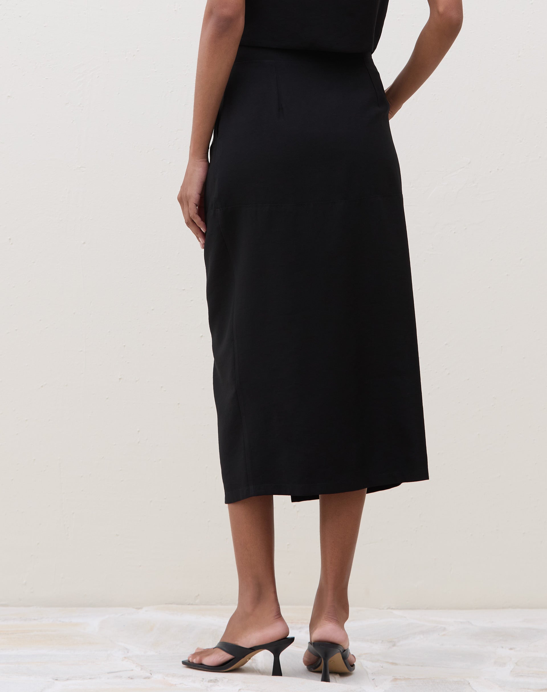 Vista traseira da saia midi preta, destacando o caimento do tecido.
