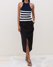 Modelo vestindo saia midi preta com fenda frontal e blusa listrada, em pose frontal.