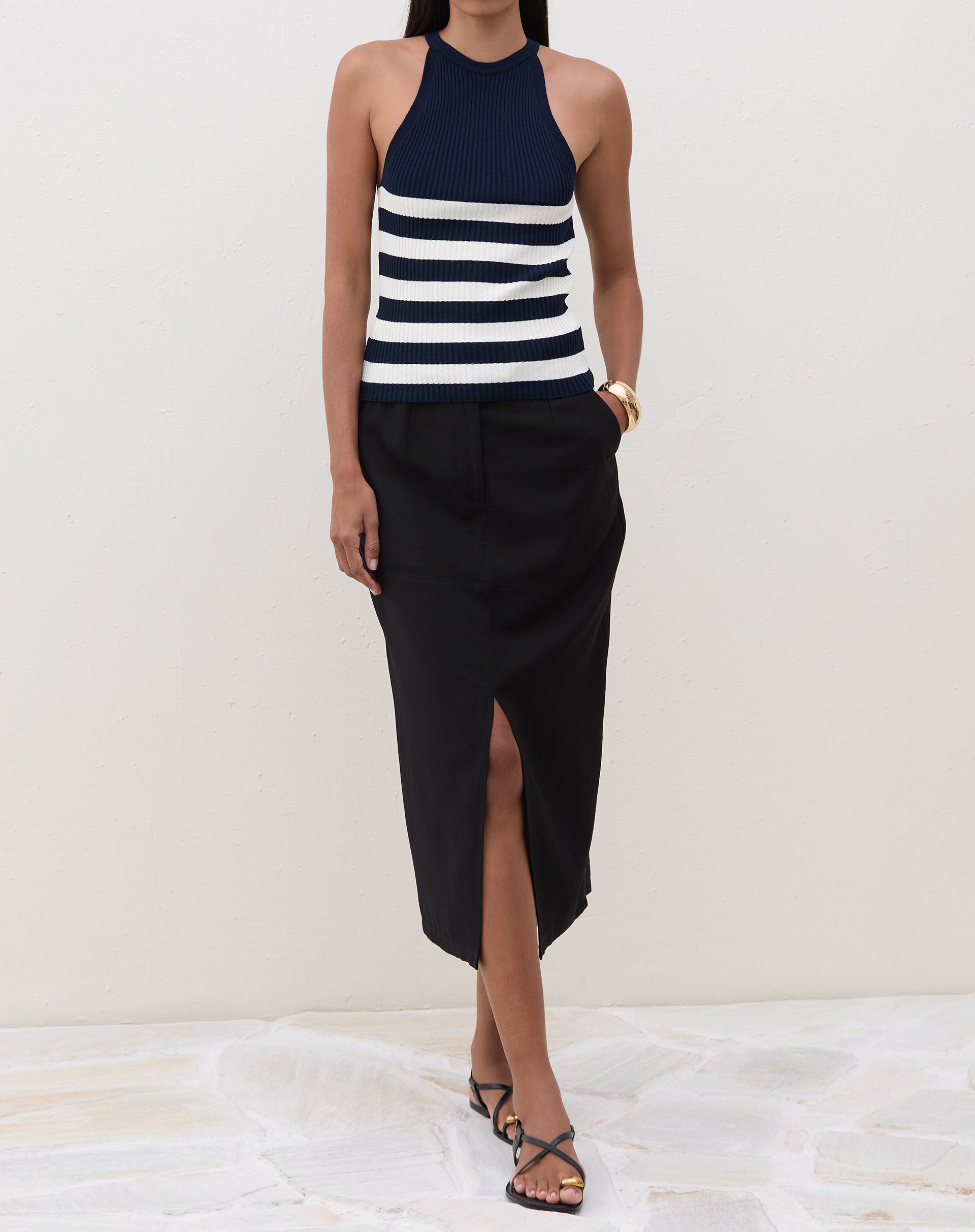 Modelo vestindo saia midi preta com fenda frontal e blusa listrada, em pose frontal.