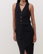 Modelo vestindo colete preto de alfaiataria com decote V, combinado com saia lápis preta.