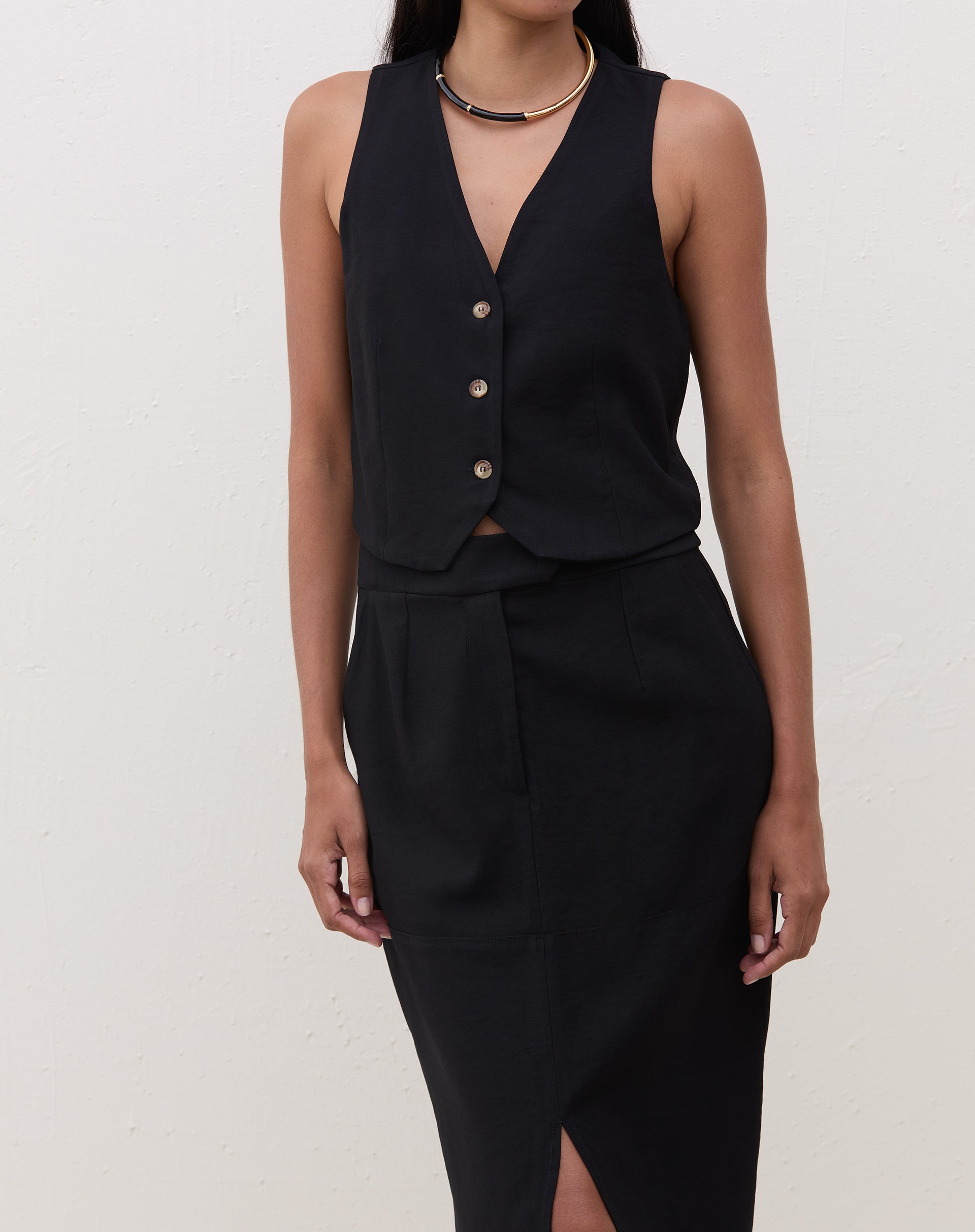 Modelo vestindo colete preto de alfaiataria com decote V, combinado com saia lápis preta.