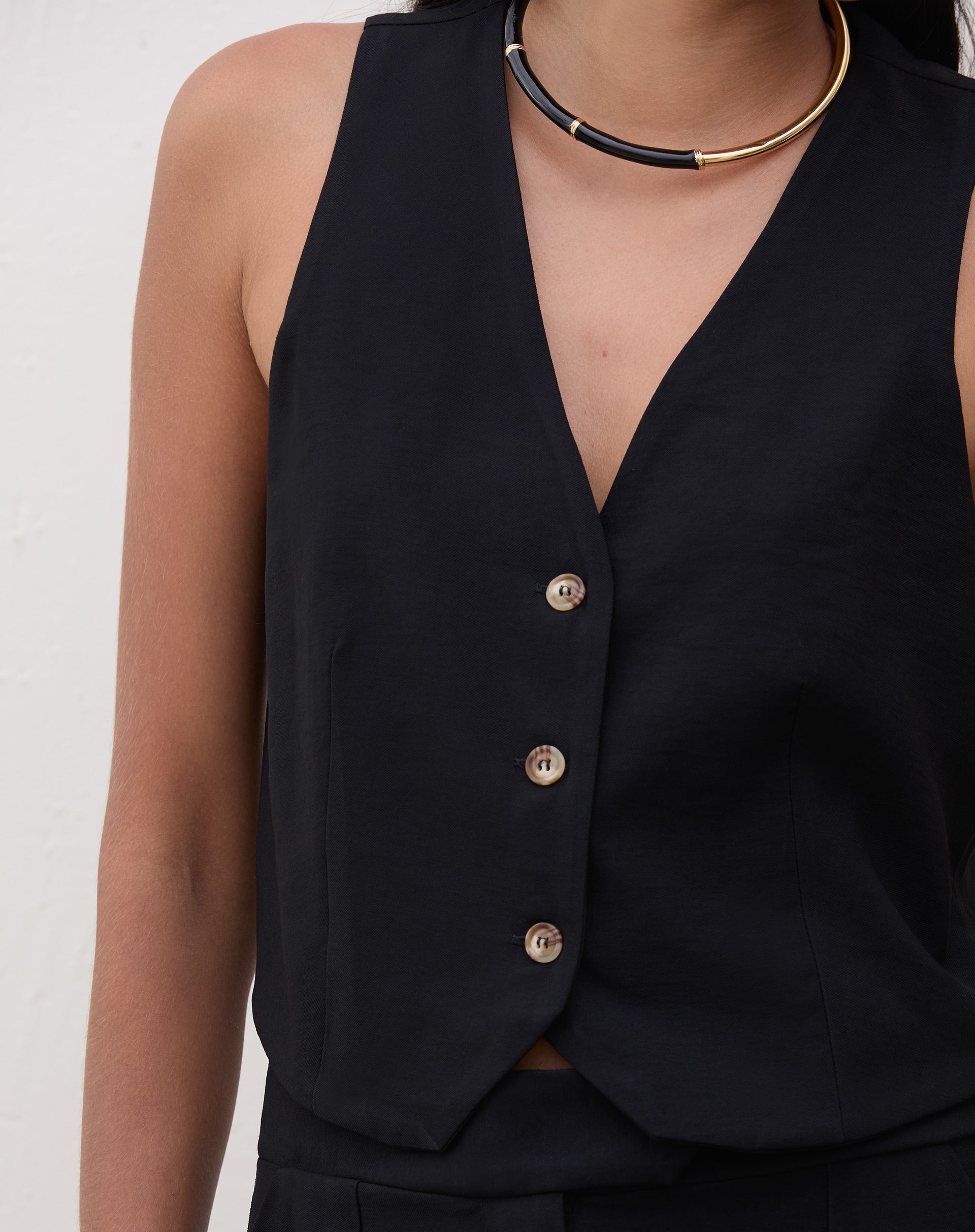 Close-up do colete preto mostrando detalhes do decote V e botões.