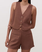 Modelo vestindo colete de alfaiataria marrom com decote em V e shorts combinando.