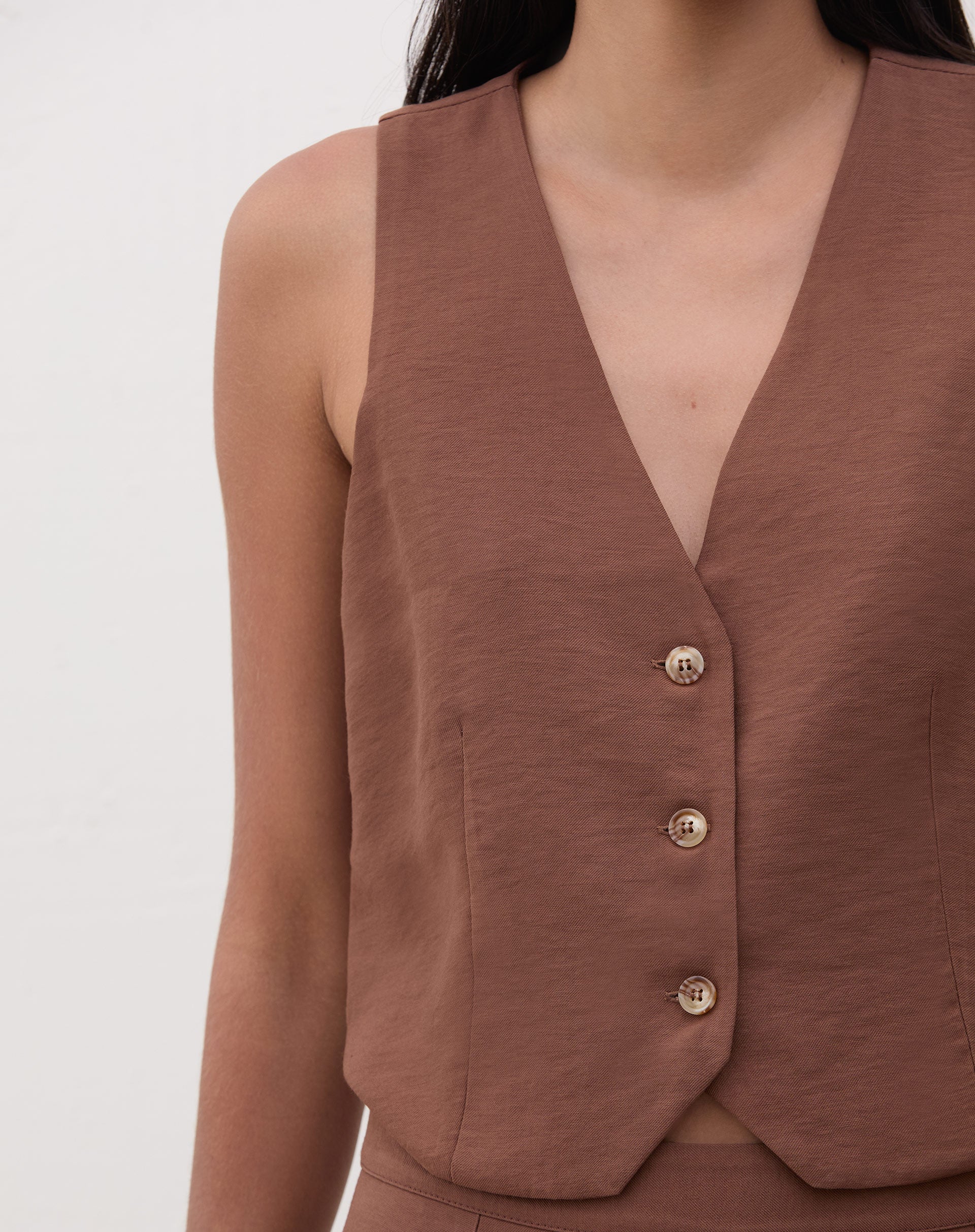 Close-up do colete de alfaiataria marrom com detalhes de botões.