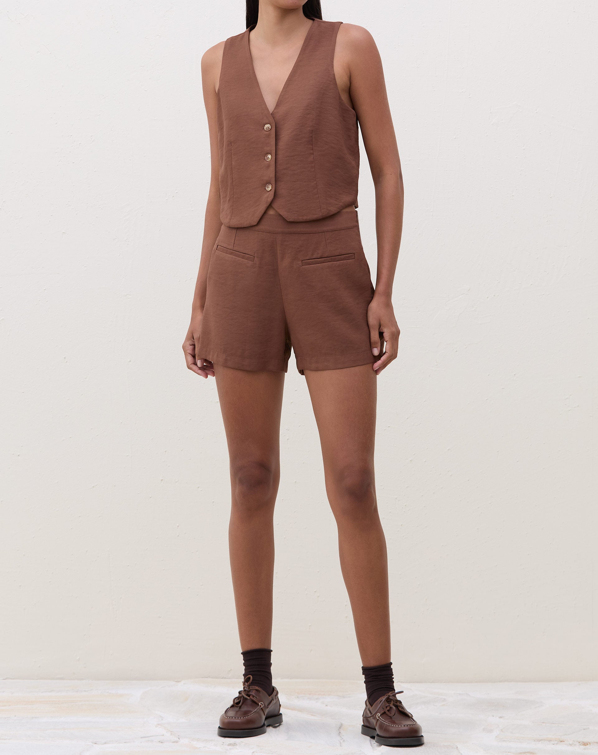 Vista frontal do conjunto com colete de alfaiataria marrom e shorts.