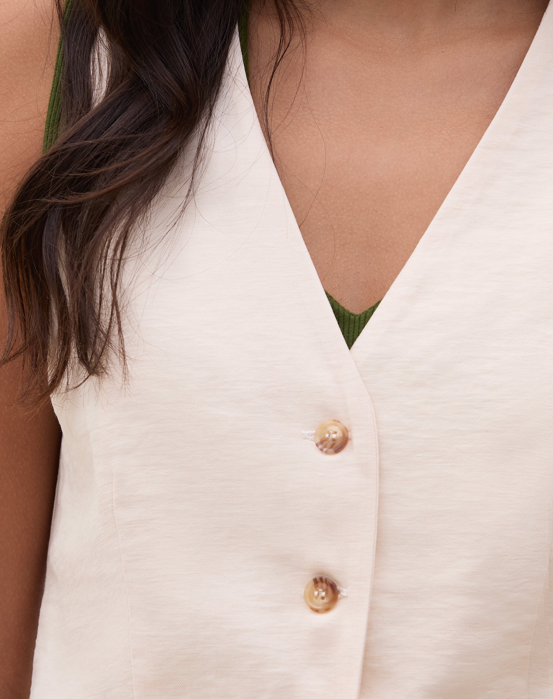 Detalhe do decote em V do colete de alfaiataria bege.