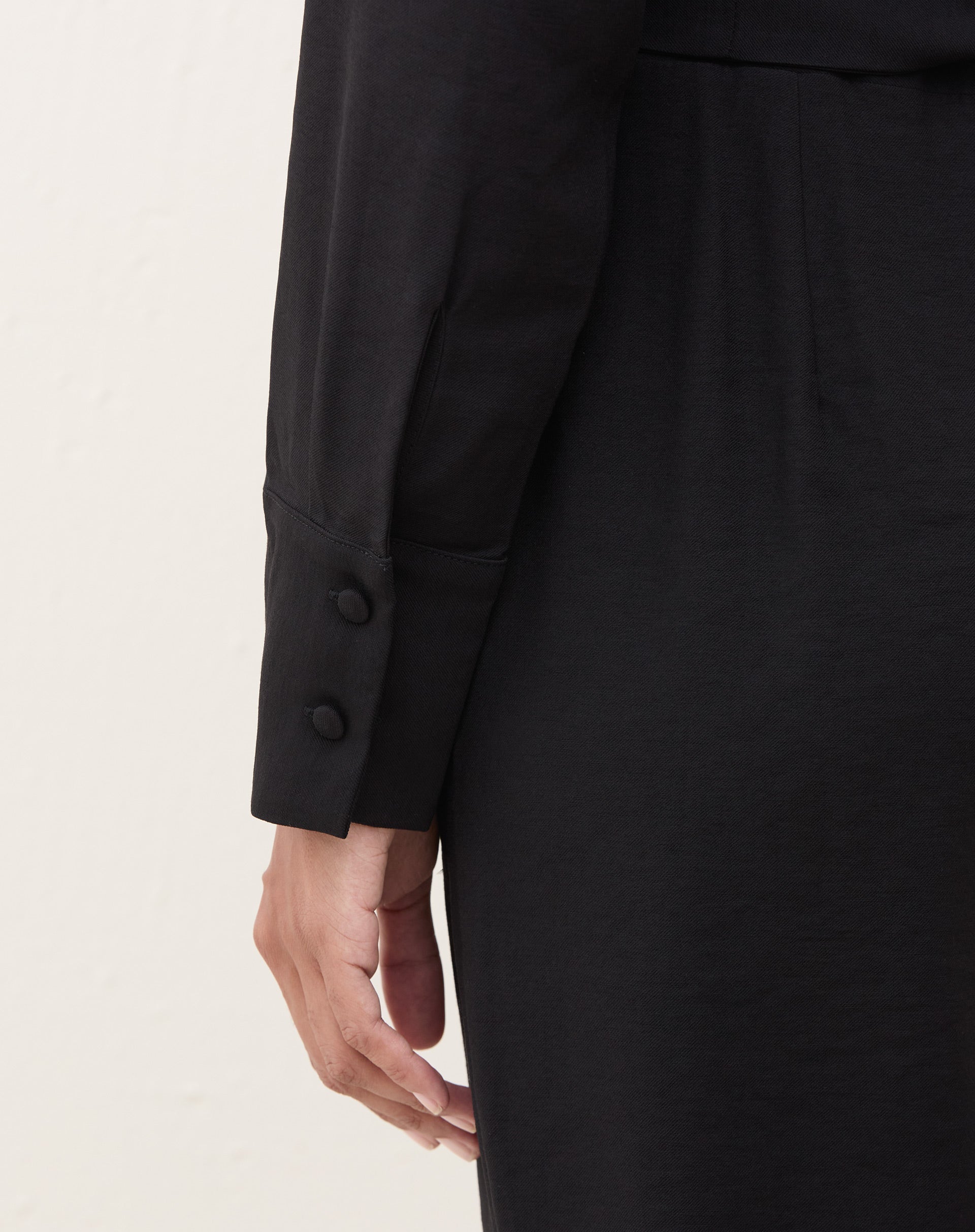 Vista lateral do macacão preto com manga longa e bolsos laterais.