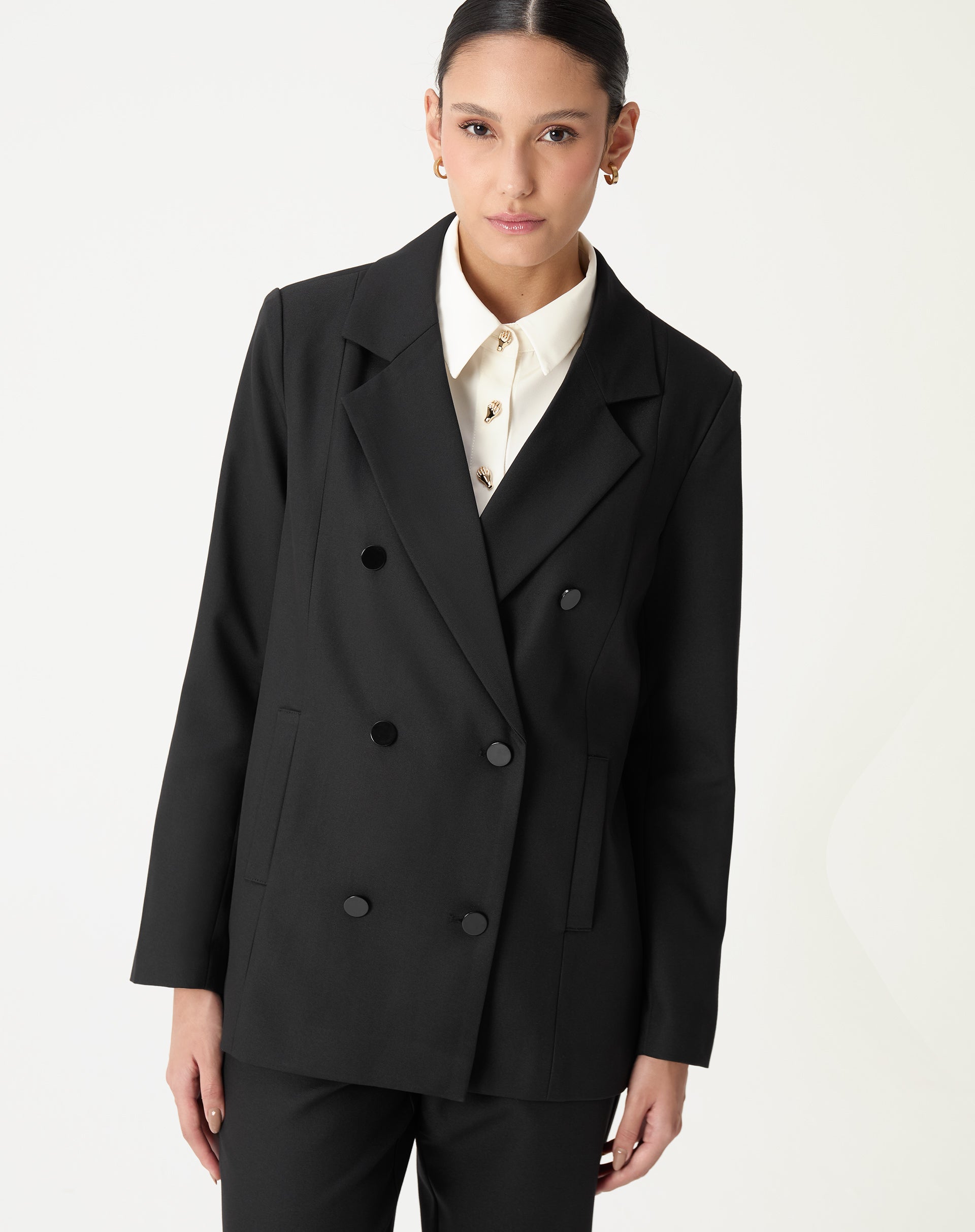 Imagem 3/4 frontal do blazer oversized preto usado sobre camisa branca com botões decorativos, visual de alfaiataria feminina.