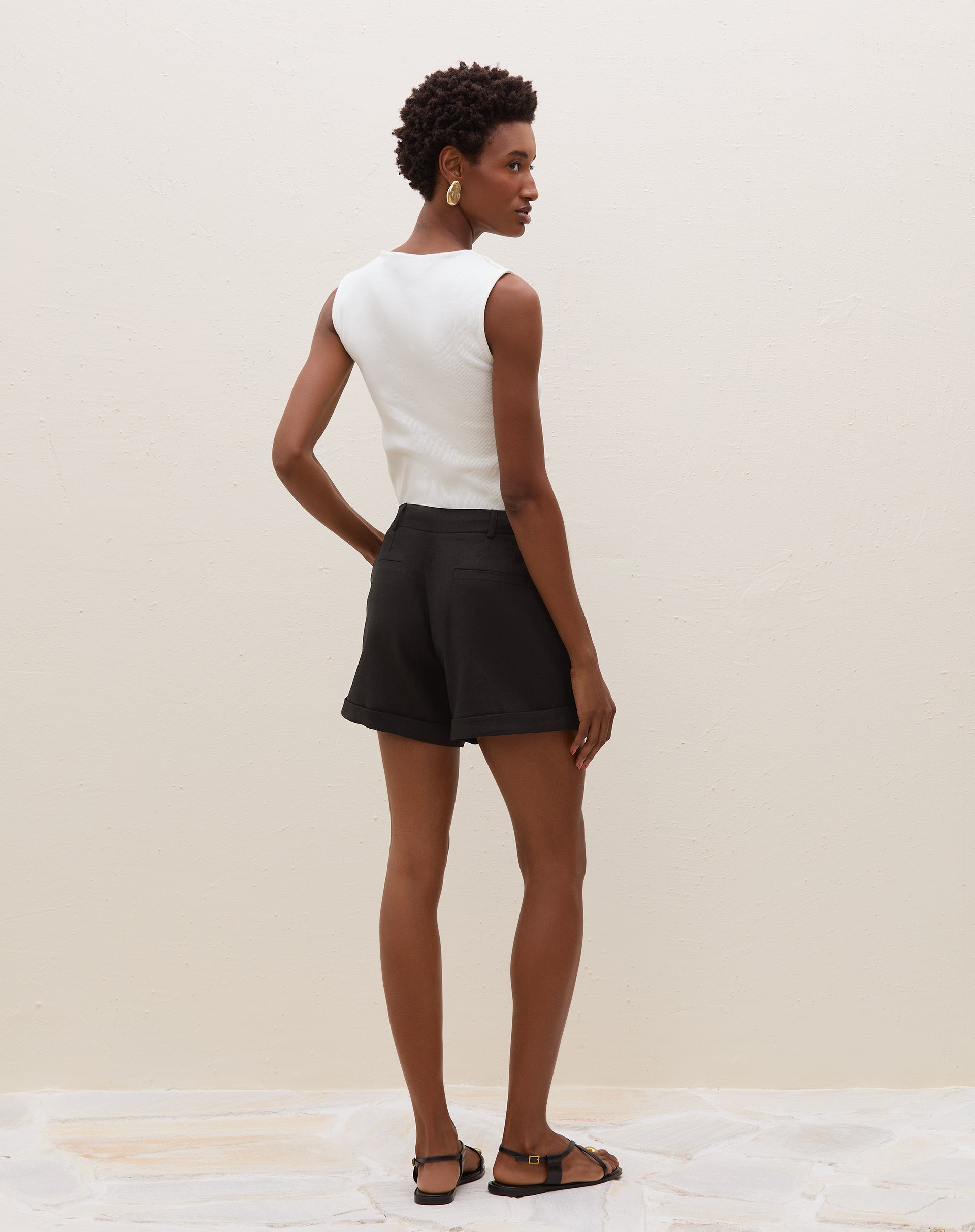 Vista traseira do shorts preto de alfaiataria, mostrando os bolsos e o acabamento da barra dobrada.