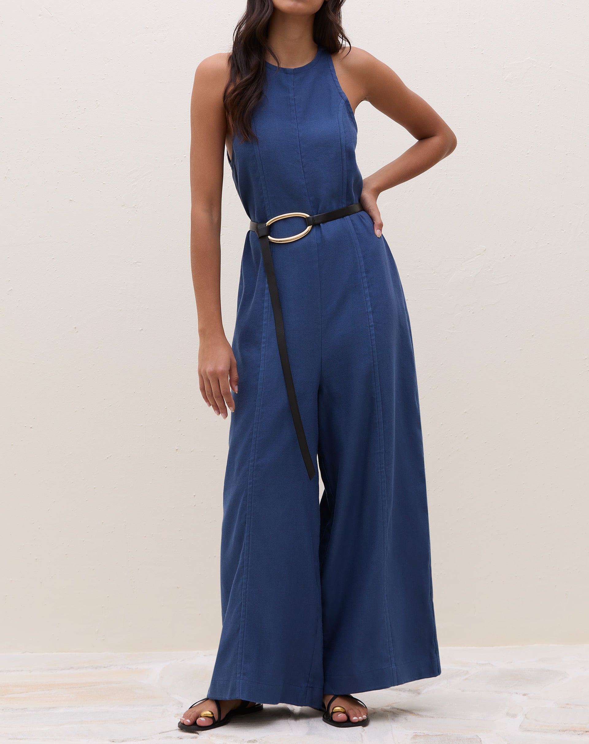 Macacão azul com decote halter e cintura ajustada por cinto, visto de frente.