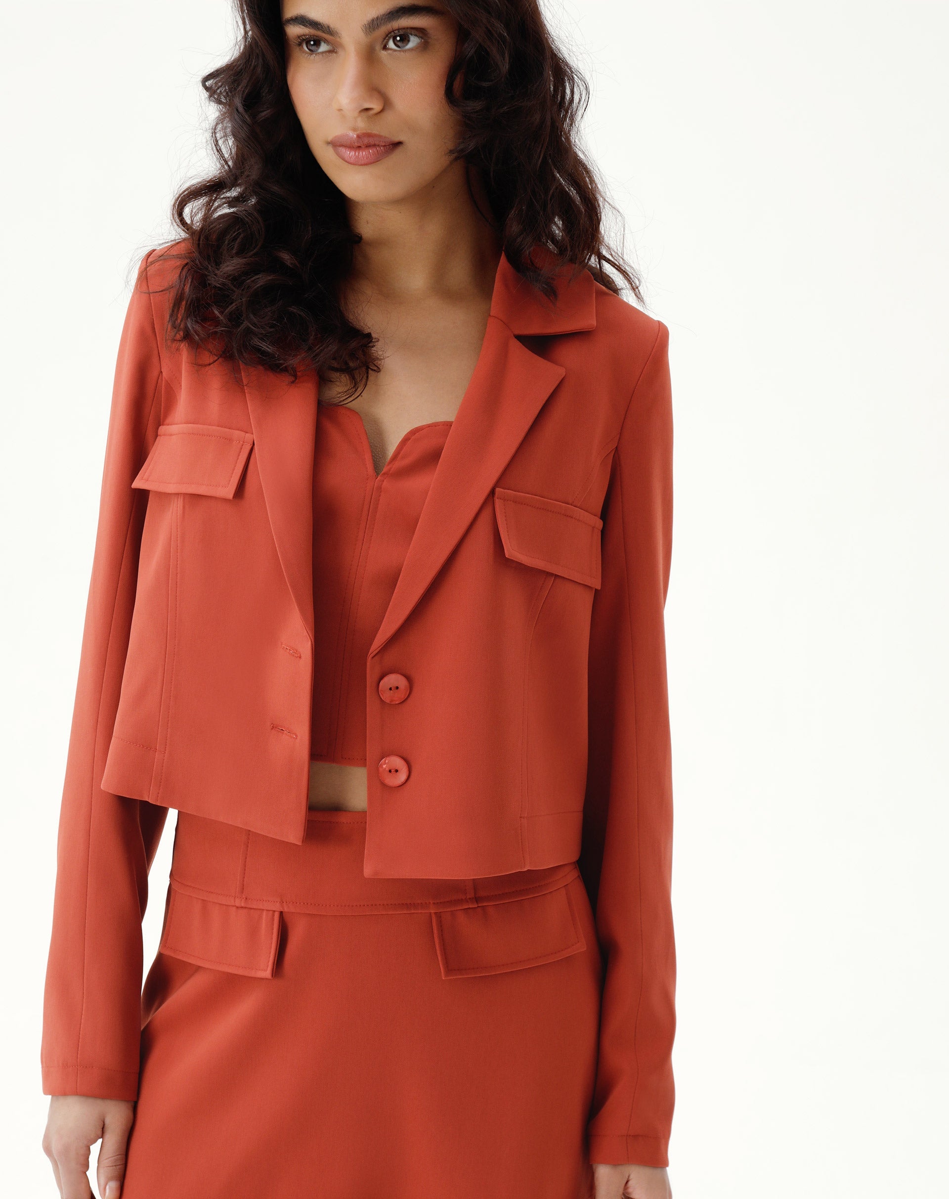 Blazer cropped marrom com bolsos e lapela entalhada, visto de frente.