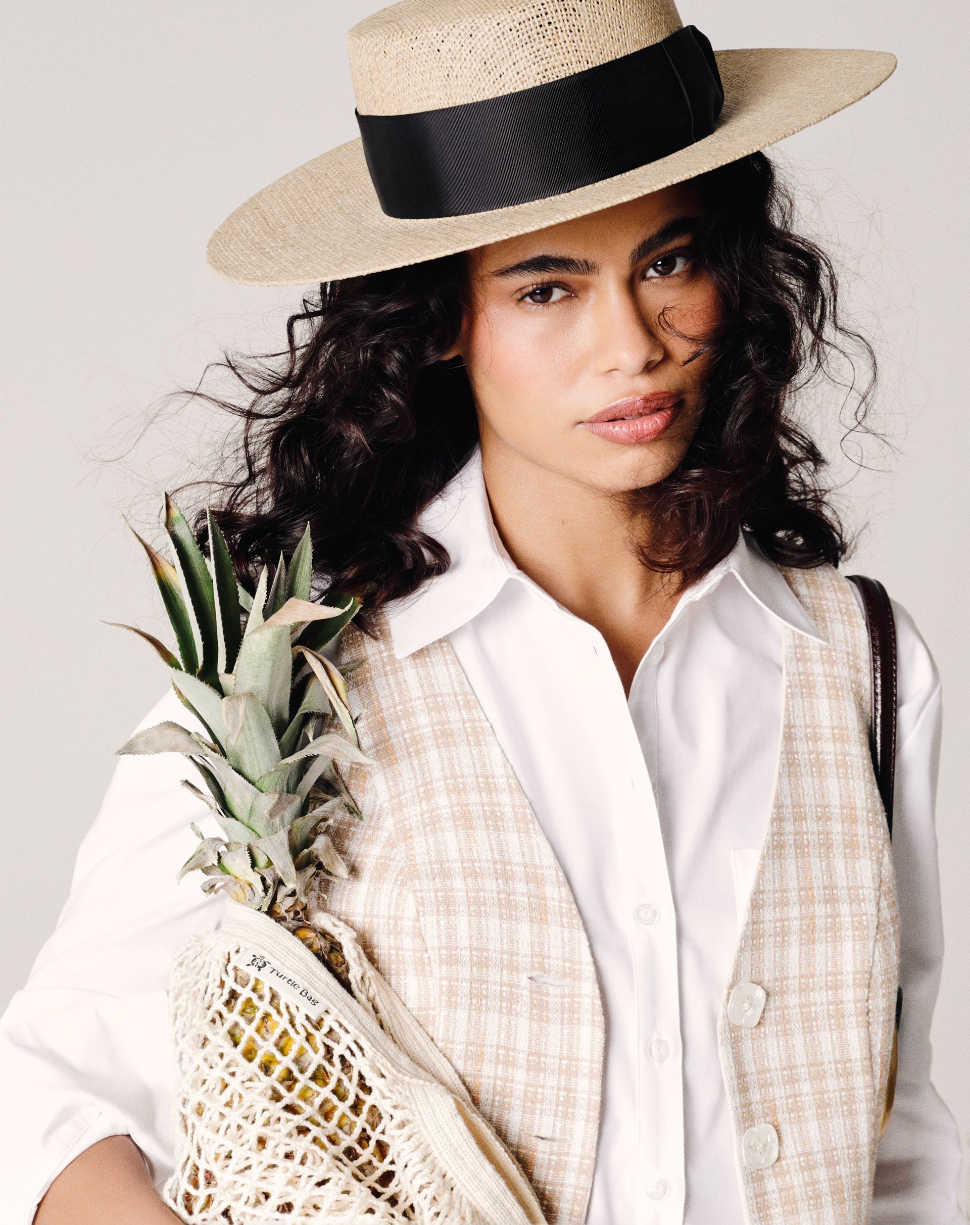 Modelo vestindo colete de alfaiataria com decote em V e estampa xadrez, segurando um abacaxi.