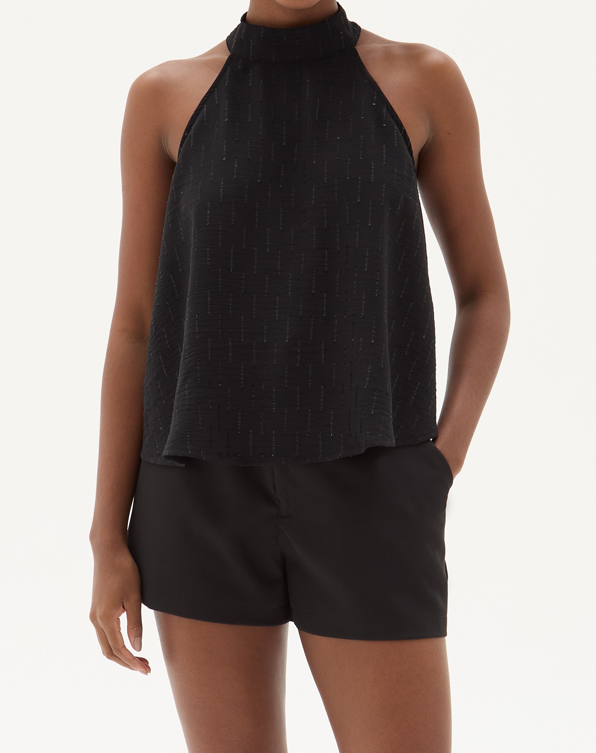 Modelo vestindo shorts curto reto de alfaiataria preto com blusa sem mangas e botas, vista frontal.