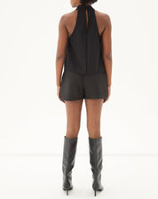 Modelo vestindo shorts curto reto de alfaiataria preto com blusa sem mangas e botas, vista traseira.