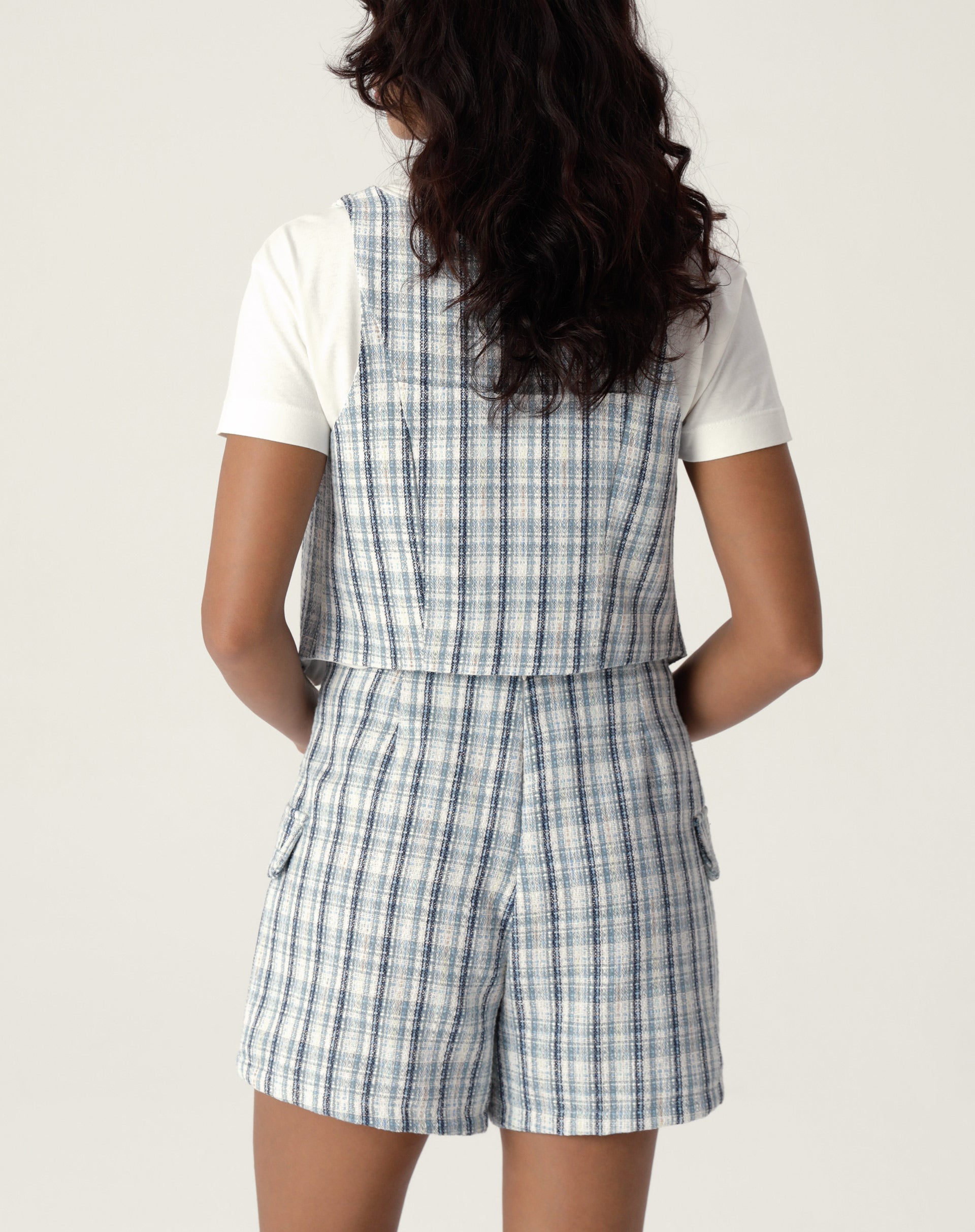 Detalhe do shorts frente transpassada de alfaiataria com estampa xadrez, evidenciando o acabamento e os bolsos.